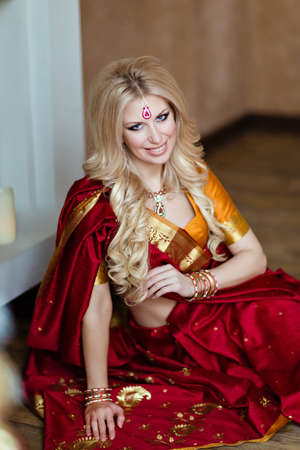 Beautiful and sensual blonde girl in Indian red saree sitting on the floorの写真素材