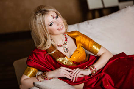 very beautiful and sensual blonde girl in Indian red Sari lying on the sofaの写真素材