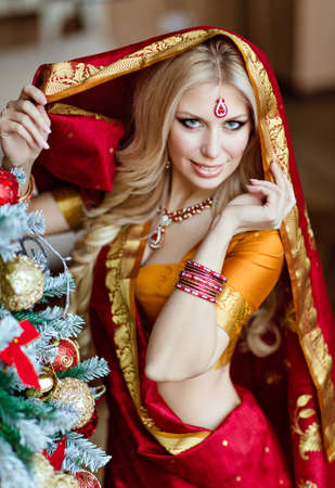 Beautiful and sensual blonde girl in Indian red saree around the Christmas treeの写真素材
