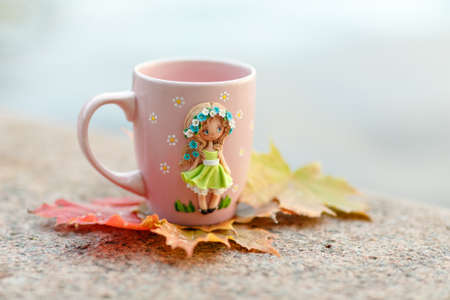 Pink mug with decorations in the form of a girl in a dress made of polymer clay on nature backgroundの写真素材