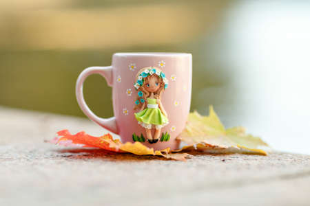 Pink mug with decorations in the form of a girl in a dress made of polymer clay on nature backgroundの写真素材