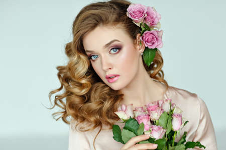 Portrait of a beautiful blonde girl with delicate pink roses on a light background in the studio. Close-upの写真素材