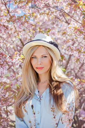 Portrait of a beautiful blonde girl with long hair and a hat in a blue dress smiling on the...
