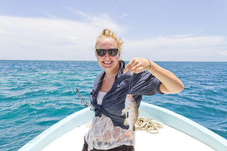 Woman holds up a fish that she caught deep-sea fishing on the oceanの写真素材