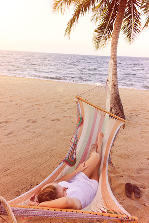 Woman relaxing in a hammock on a beach next to a palm treeの写真素材