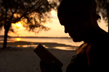 Silhouette of a woman sitting on the beach and reading a bookの写真素材