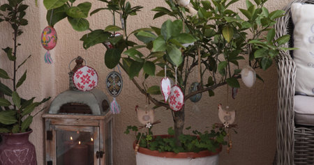 Colorful Easter egg decorations dangle from a vibrant Easter tree adorned with lush greenery. The...