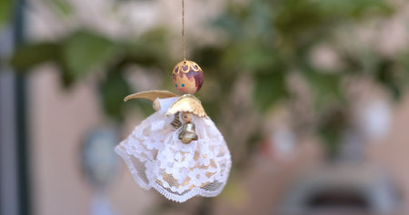 A handcrafted angel decoration dangles from a thin string, featuring a beautiful lace skirt and golden accents. Bright greenery serves as a backdrop, creating a peaceful atmosphere.の写真素材