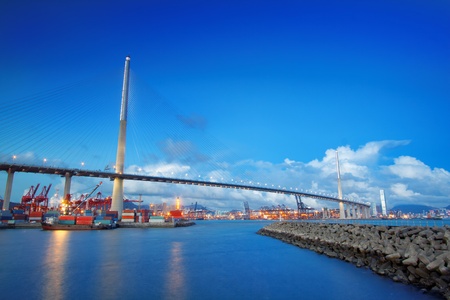 Port warehouse with containers and industrial cargoes , view under bridge on water break at sunsetの写真素材