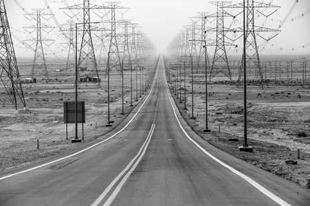 Stright road flanked on both sides with highvoltage power lines in black and whiteの写真素材