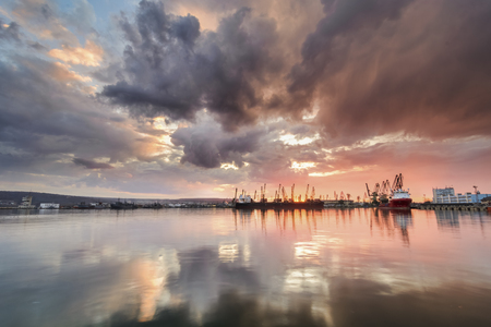 Silhouette of port cranes against a dramatic sky at sunsetの写真素材