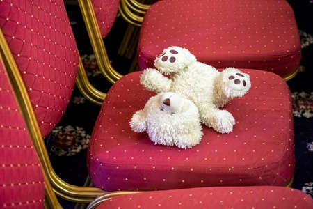 white teddy bear forgotten on a red chair.の写真素材