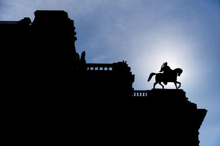 Silhouette of man on horse statue on top of a Vienna's building with sun directly behind, blue sky...