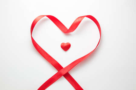 Small red heart in the center of red ribbon placed in a shape of heart, on isolated white background; lots of white space, perfect for valentine or special occasion useの写真素材