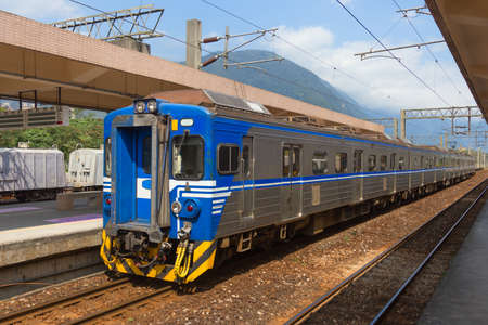 Taiwan train parks at a station on a sunny day with blue sky and mountains in background