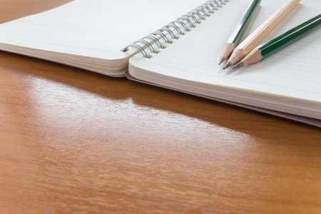 Three pencils on top of open notebook with blank pages on wooden table, selective focus on tips of pencils with blur foreground and backgroundの写真素材