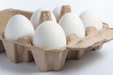 Six white eggs in recycled brown paper container on white backgroundの写真素材