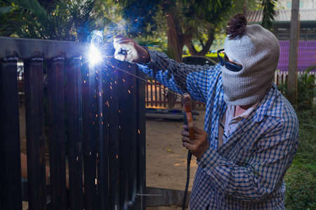 A man wering cloth mask and sunglasses welding steel platform outdoor in late evening