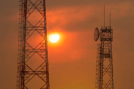 Communication tower against warm color of morning sunrise with soft flowing fluffy clouds