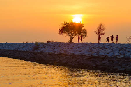 Sunset with colorful sky at a beach in Pattaya, Thailand with silhouette of people and small trees on rocky pier against colorful sunset skyの写真素材