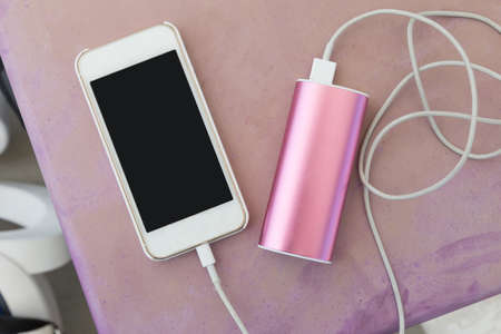 mobile phone in plastic case plugin to a power bank charger through a charging cable, on old pinkish purple outdoor plastic tableの写真素材