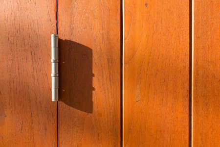 Close up of old and weathered wood panel with metal hinge in afternoon light showing cast shadowの写真素材