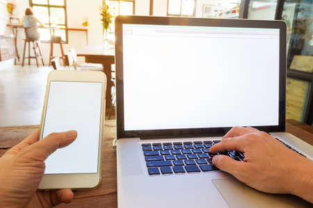 man working using computer and phone in a coffee shop, looking out the brightly lit windows and door with bright warm light and flare in the frame, selective focus on keyboardの写真素材
