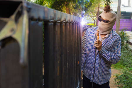 Unidentified hooded man welding steel platform, bright light and sparks, outdoor with blur background treesの写真素材