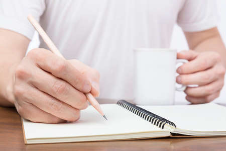 Close up of businessman's hand holding a pencil to write on an empty notebook and holding a cup of...