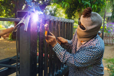 Unidentified hooded man welding steel platform, bright light and sparks, outdoor with blurr background treesの写真素材
