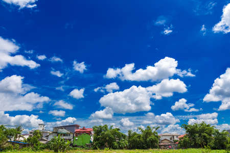 Deep blue sky with bright white clouds with foreground green fileds and houses in northern Thailandの写真素材