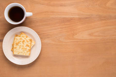 Mobile phone, paper notebook, pencil plate of crackers, and cup of coffee or tea are arranged in simple flatlay design on wood table with copyspace on topの写真素材