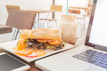 Smoked salmon sandwich, drink, laptop computer, smart phone in a restaurant with bright soft lightの写真素材
