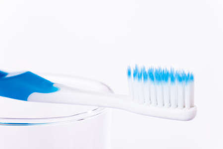 Toothbrush with blue color indicator on end of extra thin bristle's tips laying on clear glass cup against white background, selective focusの写真素材
