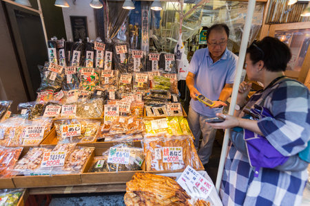 TOKYO, JAPAN - 18 JULY 2016 - Seafood snack vendor shows his customer the price in his shop in Tsukiji Fish Market, Tokyo, Japan on July 18, 2016.のeditorial素材