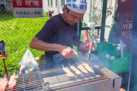 TOKYO, JAPAN - 18 JULY 2016 - Street vendor man cooks fish on sticks at Tsukiji Fish Market in Tokyo, Japan on July 18, 2016のeditorial素材