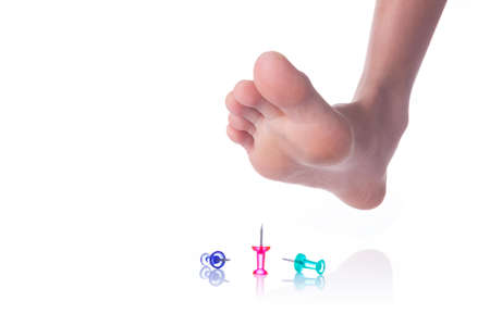 Person foot about to step on sharp push pins, on white background, showing danger concept