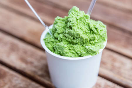 Green tea ice cream in a white paper cup on outdoor lawn table, selective focus on ice creamの写真素材