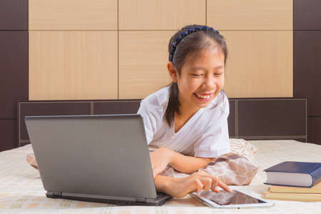 Happy Asian female teenager using technology, interacting with moblie computer tablet device in her...