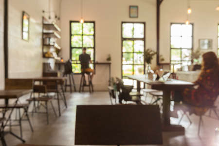 Blurred coffee shop with customers in warm vintage tone, showing bright sunny outdoor through large size glass windows and doorの写真素材