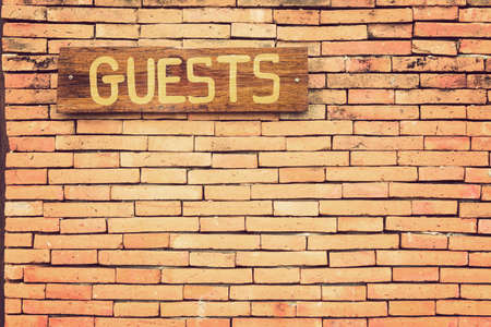Wooden Guests sign on terracotta brick wall with retro vintage color effect, room for copy spaceの写真素材