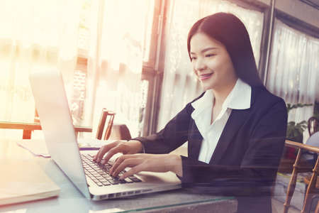 Smiling young asian executive business woman working on her computer indoor, golden hour lighting coming through the large windows, vintage retro style lookの写真素材
