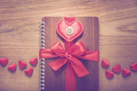 notebook wrapped with red ribbon, red felt hearts with Made With Love medal on top in vintage color tone, all on wooden tableの写真素材