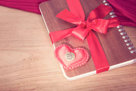 notebook wrapped with red ribbon, red felt hearts in vintage pink color tone, all on wooden table,...