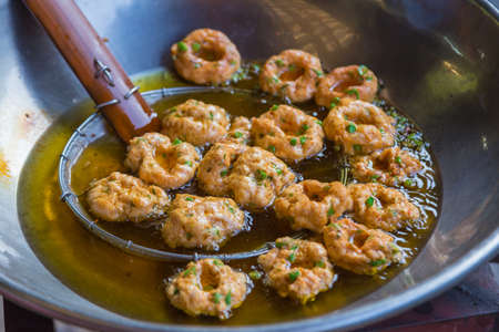 deep fried spicy fish balls, a traditional Thai dish named Tom Mun, being fried in hot oil at a local marketの写真素材