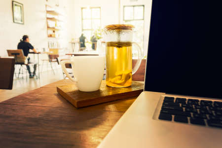 teapot, teacup, and laptop computer on wooden desk with warm sun light coming in through large windowの写真素材