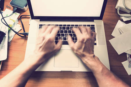 blurred male hands typing, working on computer keyboard on busy wooden desk, with vintage color tone