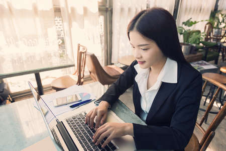 young attractive asian business woman using her computer at a coffee shop in vintage color toneの写真素材