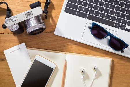 digital photography or planning photo vacation concept, showing items such as camera, computer, phone, and notebook on wooden tableの写真素材