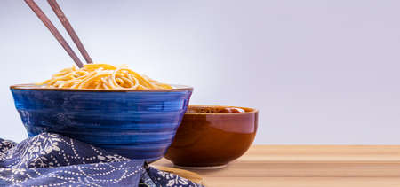 cooked Japanese wheat noodles in a blue ceramic bowl with wooden chopsticks on wooden table, room for copy spaceの写真素材